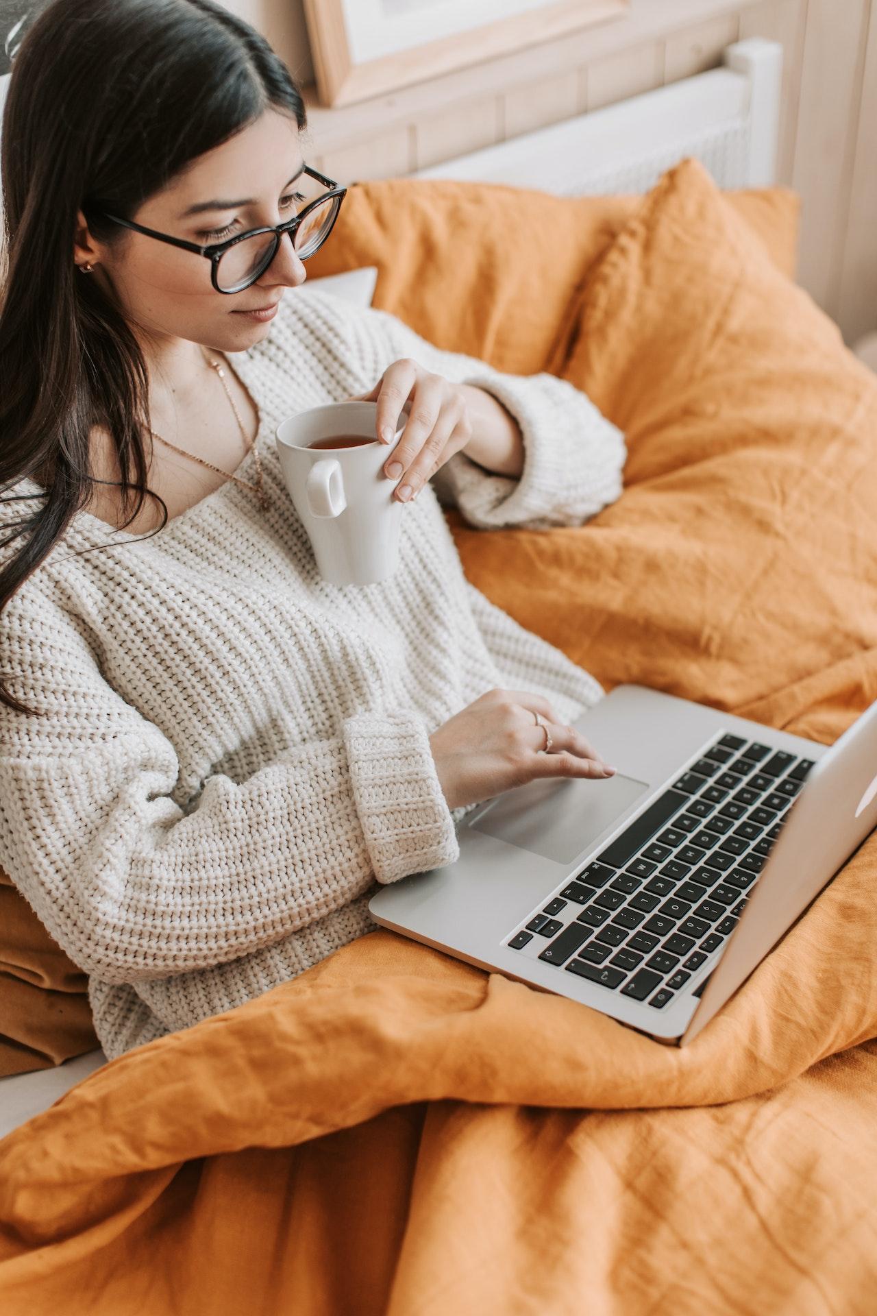 Frau sitzt im Bett mit Kaffee und Laptop